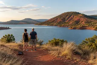 Vue réaliste du lac du Salagou, avec ses terres rouges, ses collines volcaniques et deux promeneurs accompagnés de boules de pétanque.